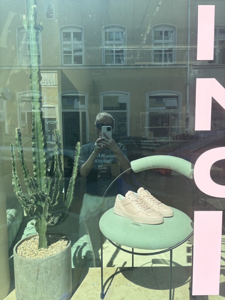 Außenansicht des VOR Stores in München mit minimalistisch gestaltetem Schaufenster, weißen Ledersneakern und großem Kaktus. Der Store zählt zu den besten Adressen für Premium- und Design-Sneaker in München.