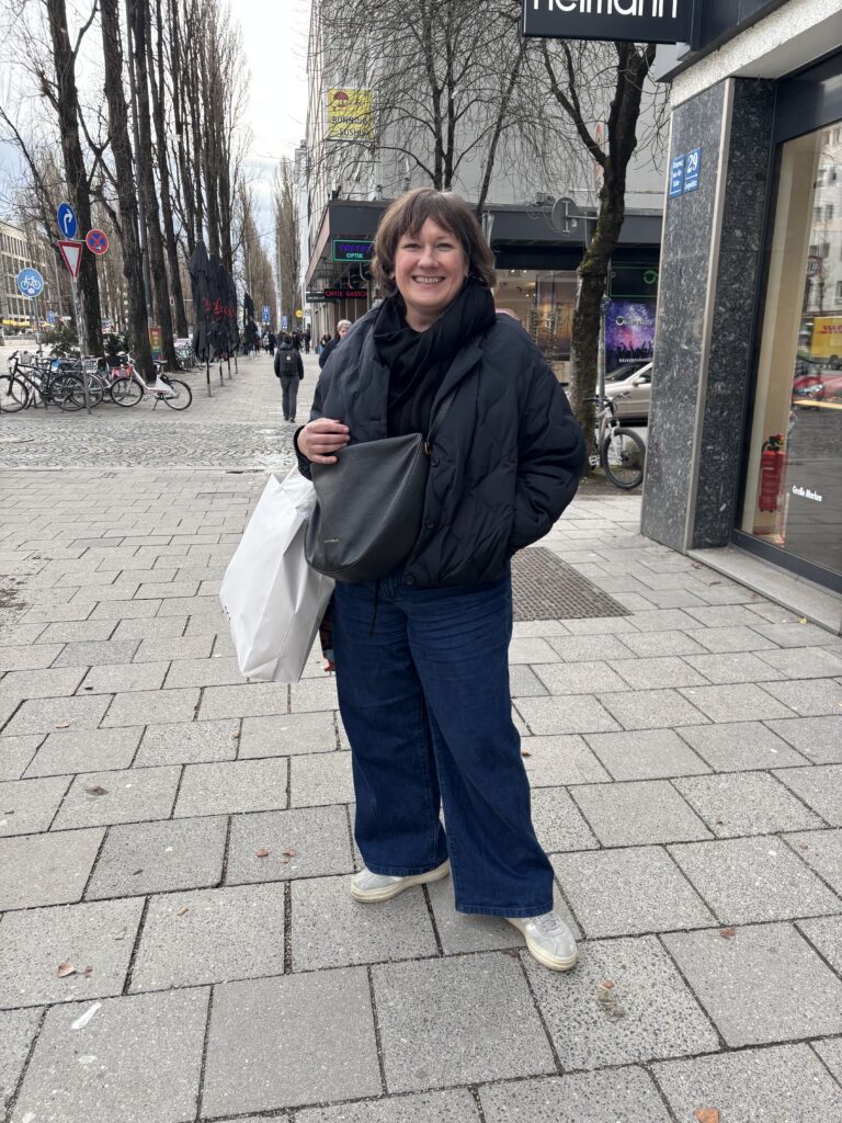 Kundin beim Personal Shopping in München mit dunkler COS Jacke, weiter Jeans und Sneakern vor einem Geschäft in der Innenstadt.