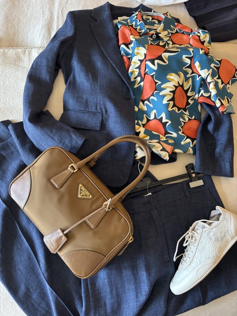 Anlass-Outfit modern kombiniert: Anzug mit Statement-Bluse und Sneakern Blauer Anzug kombiniert mit gemusterter Bluse, Sneakern und beiger Tasche – modernes Anlass-Outfit mit Basics