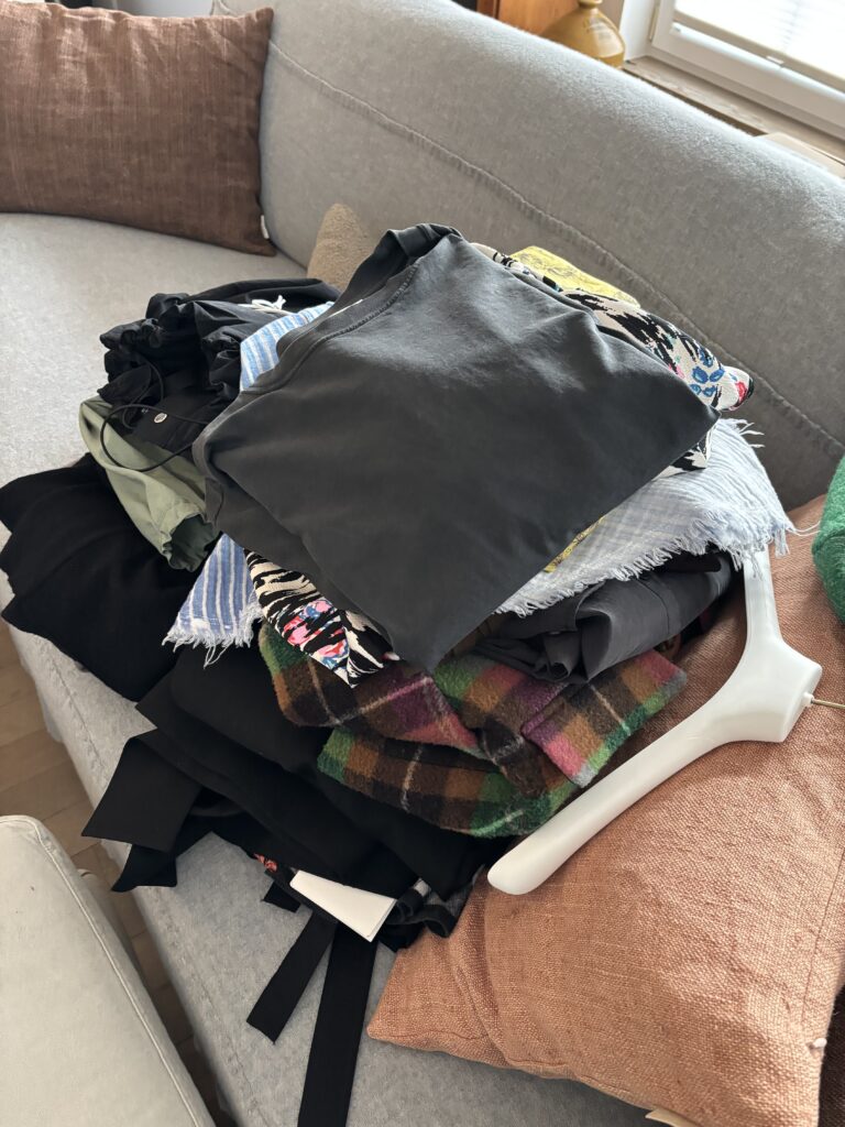 Stapel neu gekaufter Kleidung auf einem Sofa. Das Foto steht für Reizüberflutung beim Shoppen, Impulskäufe und die Schwierigkeit, gezielt passende Kleidung zu finden.