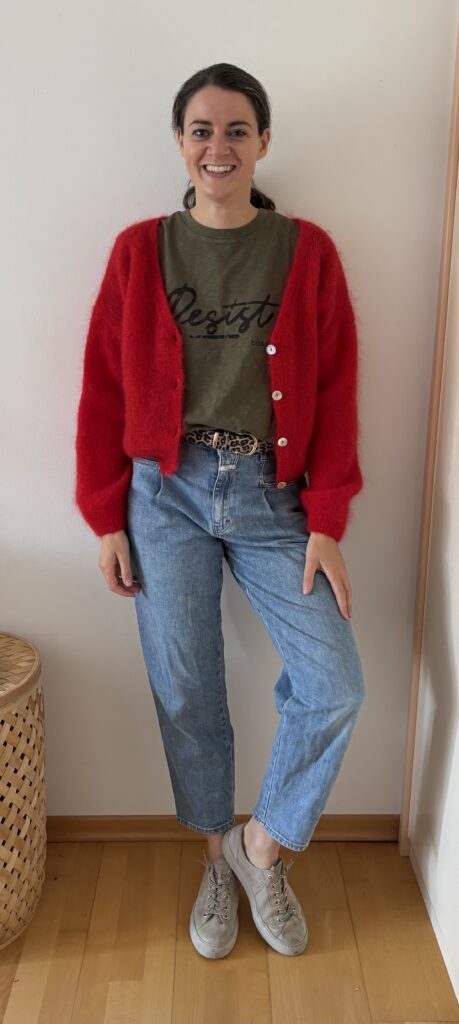 Frau in hellblauer Mom-Jeans mit hoher Taille und roter Strickjacke. Der Jeans-Schnitt eignet sich besonders für Frauen, die ihre Taille betonen und eine ausgewogene Silhouette schaffen möchten.